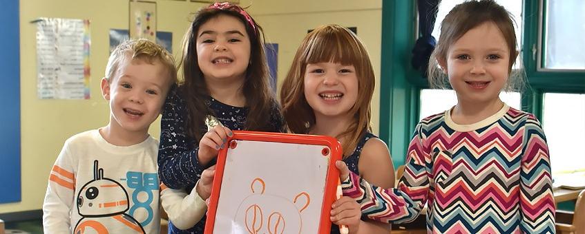 Four smiling children hold a whiteboard with a drawing on it.