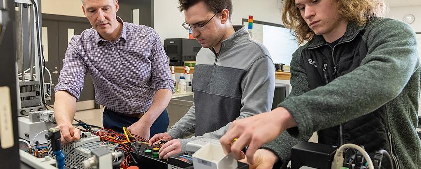 Faculty work with students and equipment in classroom lab.