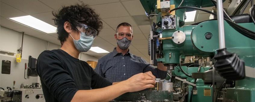 A student working on a large mechanism while being observed by an instructor.