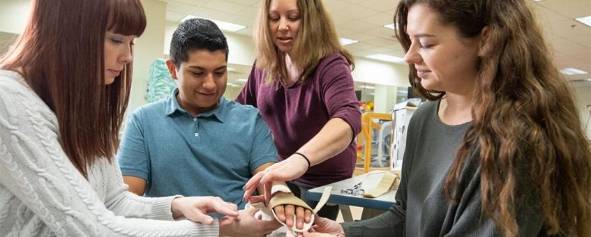 Three occupational therapy assistant students working with an instructor on how to splint a wrist.