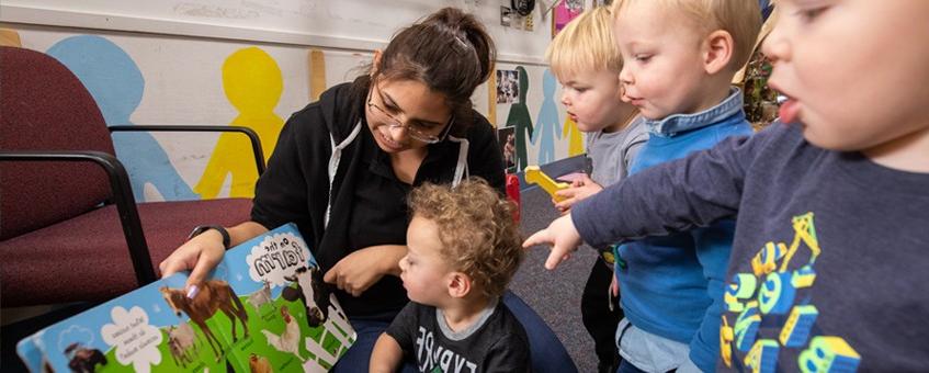 A Paraeducator student reading a picture book with four young children.